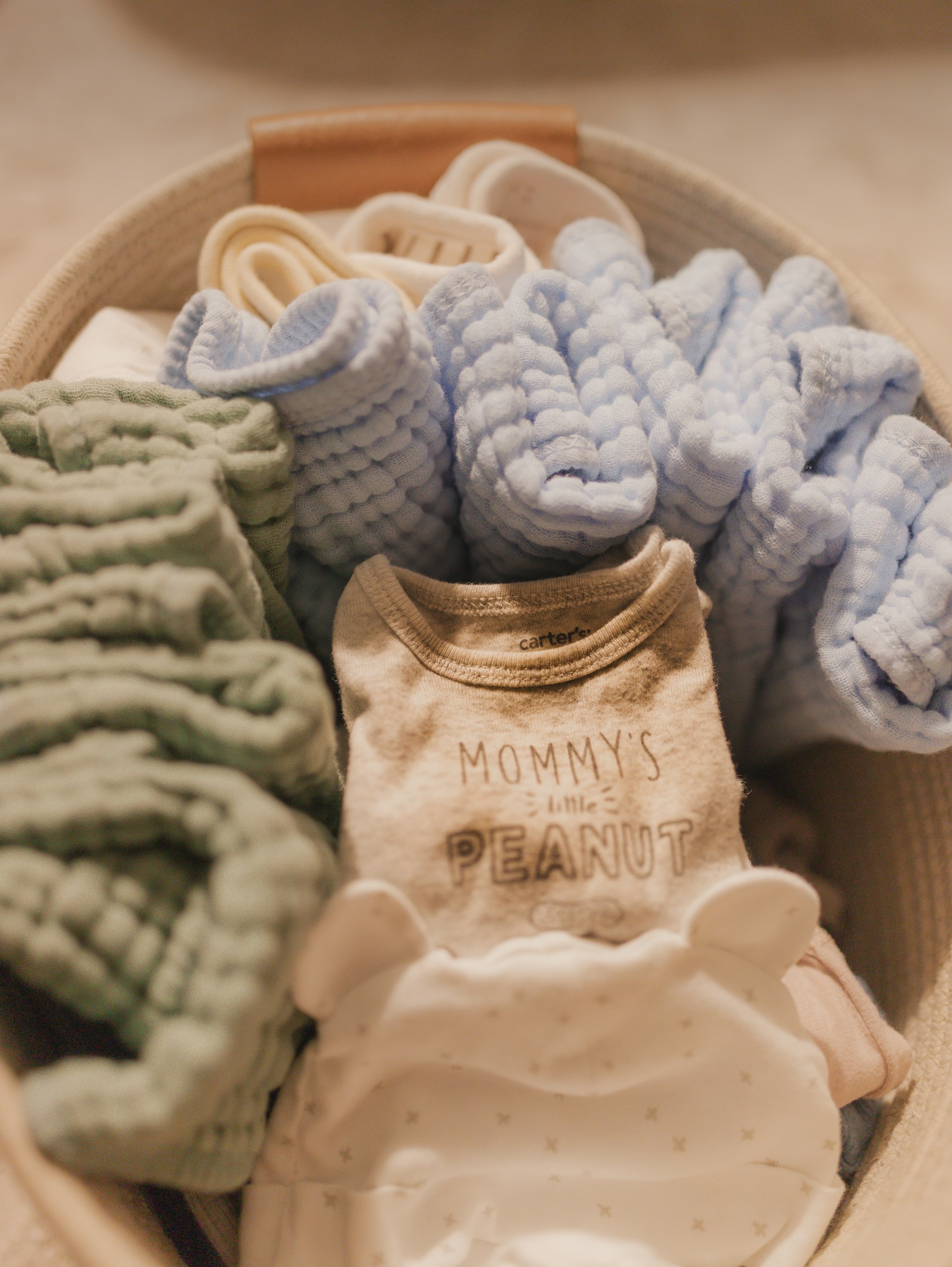 Folded baby clothes in a woven basket
