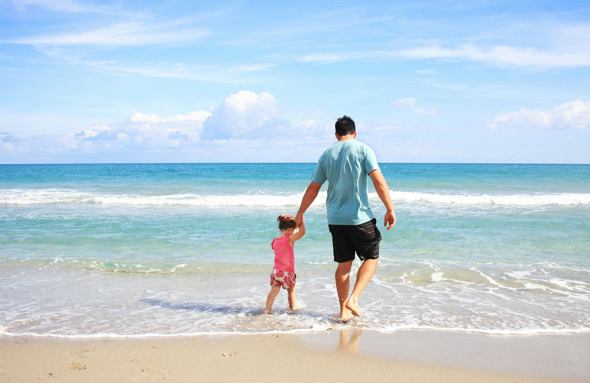 A father and young daughter walking hand in hand at the shore